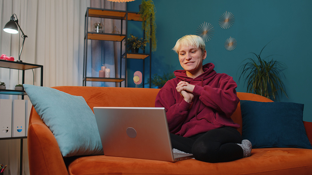 A non-binary person smiles behind a computer screen.