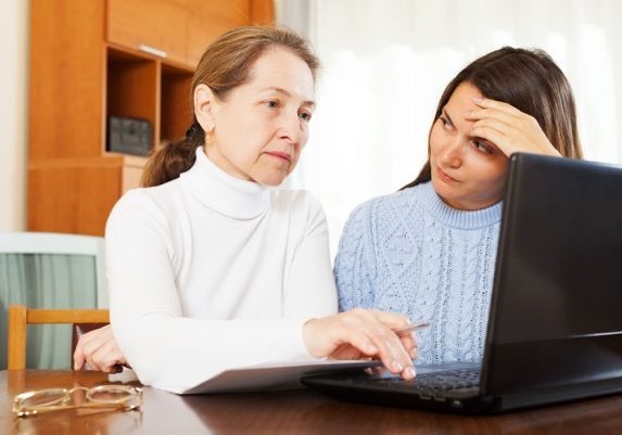 Two women sit behind a computer screen.