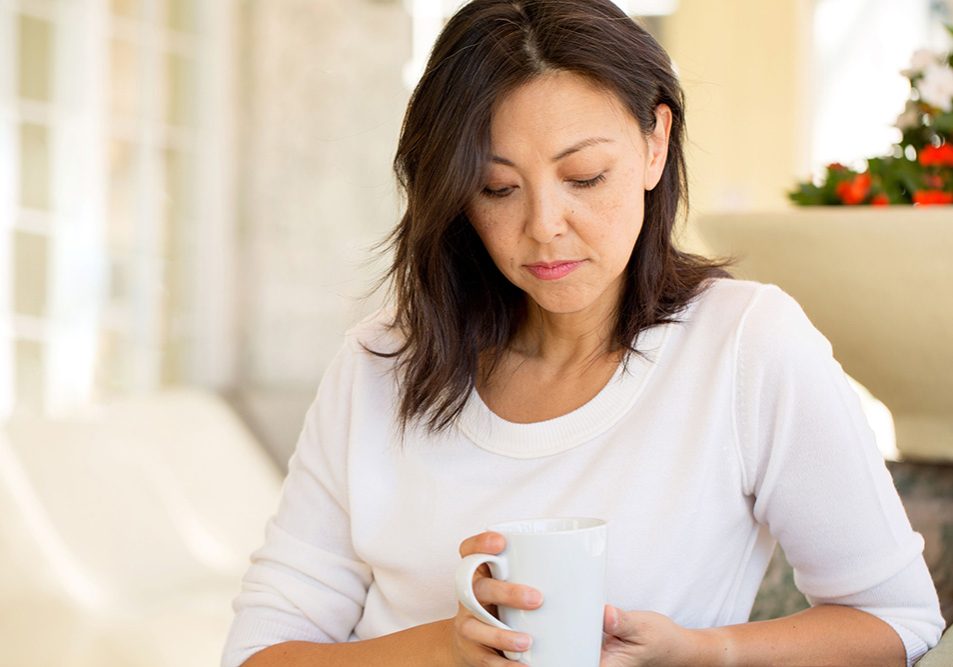 A somber middle-aged woman looks down at her coffee mug.