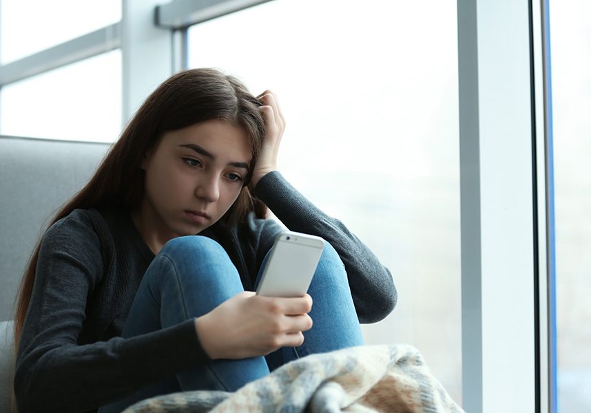 A distressed teen girl looks down at her iPhone.