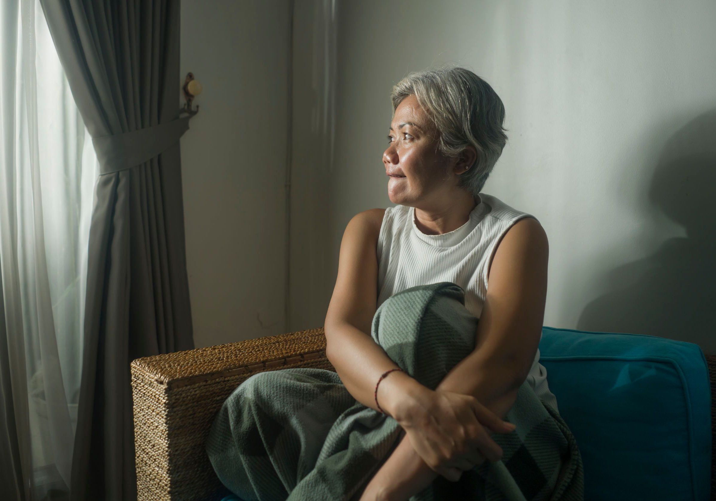 An older woman sits in solitude in a dark bedroom.