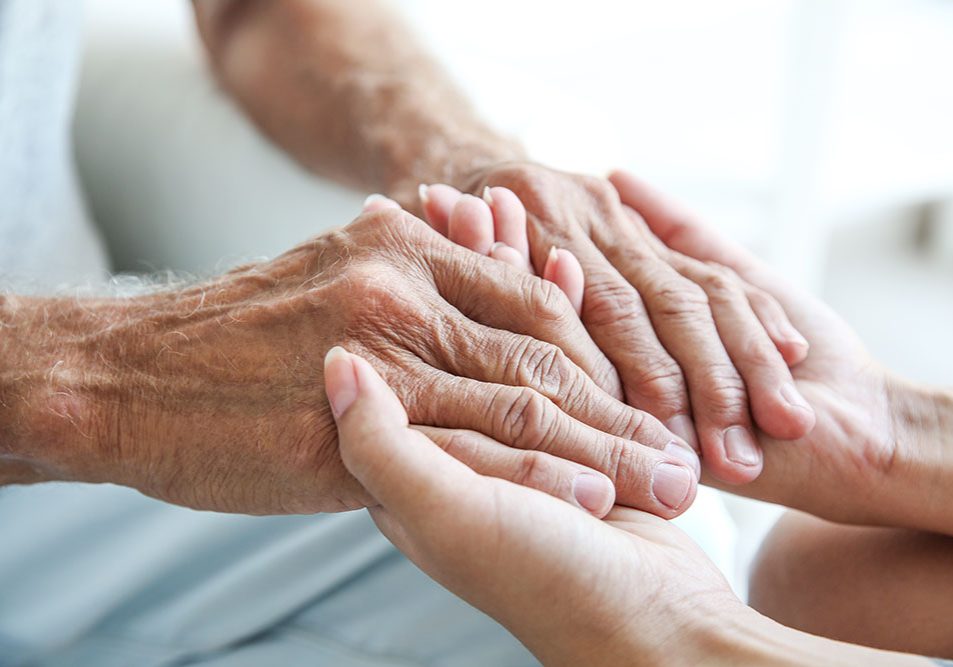 The hands of an elder held by the hands of a younger person.