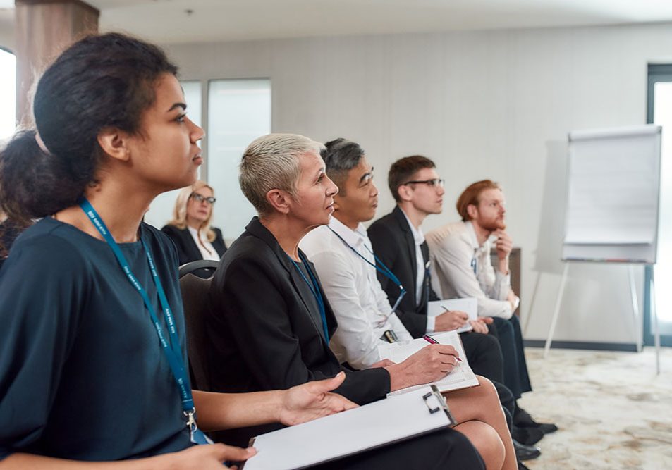 A group of professionals wearing name tags listen to a presentation.