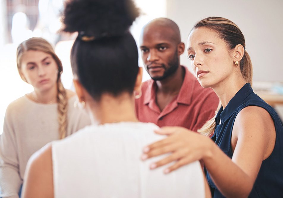 A woman places her hand on the shoulder of another woman in a support group setting.